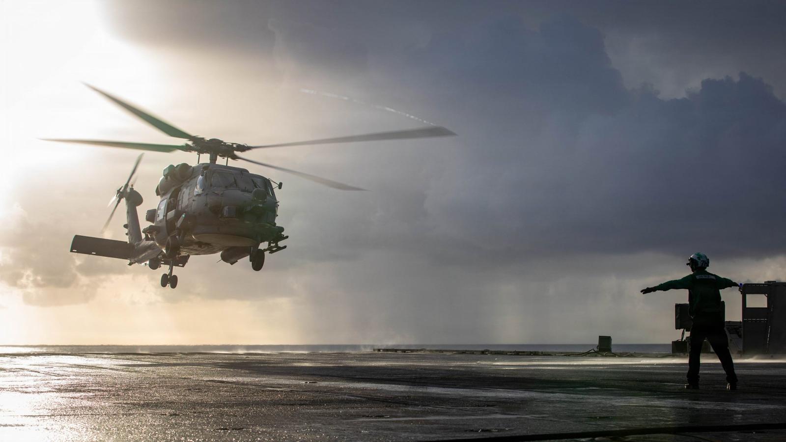Helicopter landing on ship deck at sunset.